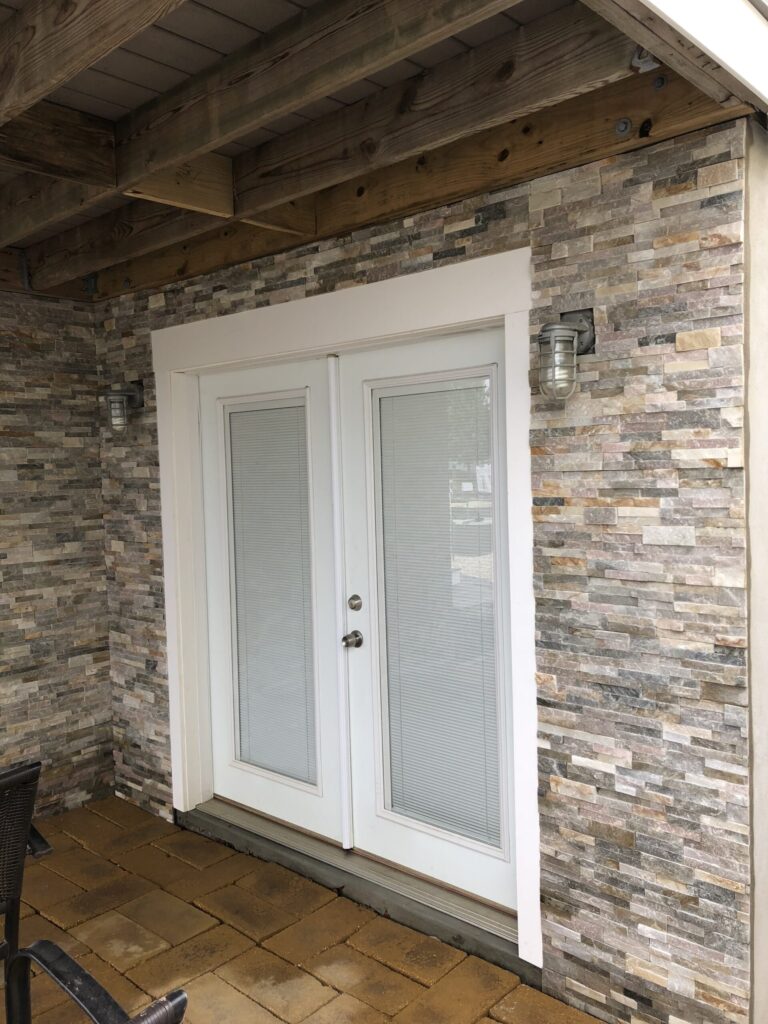 White double glass doors with blinds, surrounded by stone veneer walls and outdoor lighting on either side.