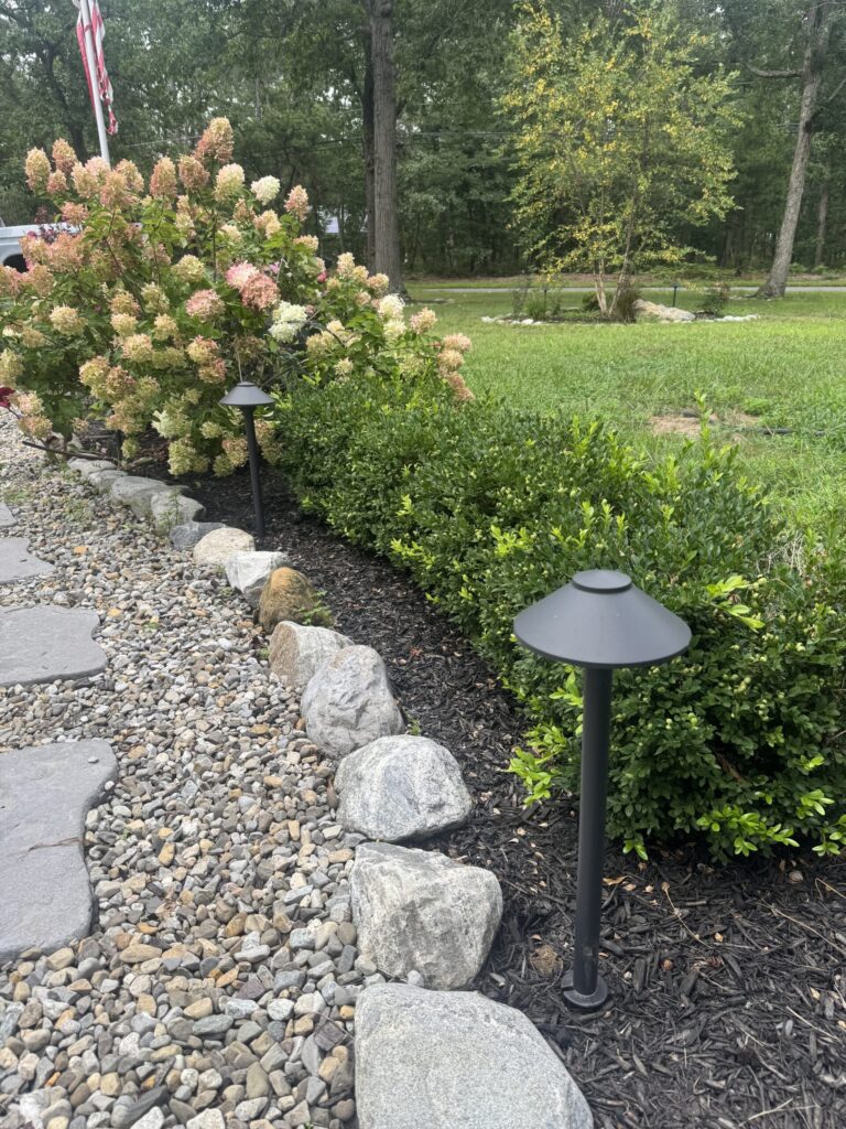 Landscape with stone walkway, solar garden lights, flowering bushes, and green lawn in the background.