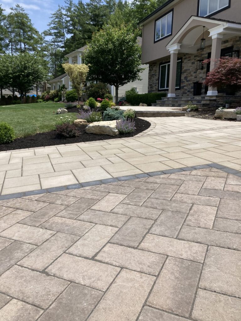 Stone pathway and patio lead to a house entrance with landscaped garden and green lawn on a sunny day.