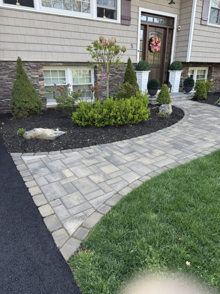 Curved stone walkway by a mulched garden bed with shrubs in front of a house with a decorated front door.